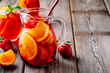Homemade red wine sangria with orange, apple, strawberry and ice in pitcher  and glass on wooden...