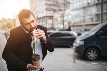 Busy man is in a hurry, he does not have time, he is going to eat snack on the go. Worker eating, drinking coffee, talking on the phone, at the same time. Businessman doing multiple tasks