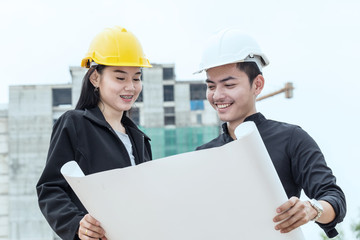 Happy Engineer man and woman looking in blueprint and discuss at construction site