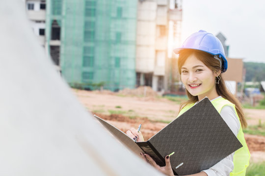 Happy Engineer woman wearing safety blue helmet smile and holding folder in construction site