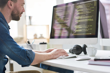 Serious pensive experienced male programmer typing code on computer while working on new software...