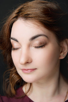 Professional make-up on closed eyes of a young brunette woman close-up on a black background. Female make-up.