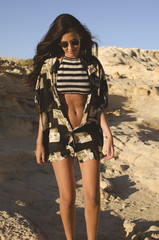  young woman with sunglasses and shirt walks carefree by a rocky coast landscape in summer