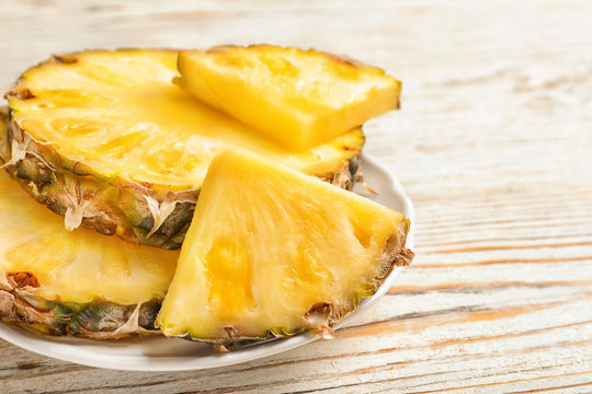 Plate with fresh pineapple slices on wooden background