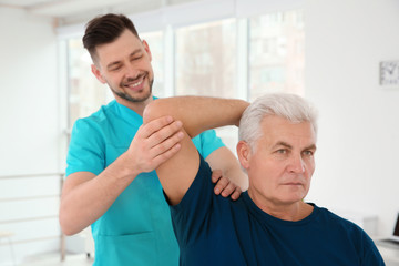 Young physiotherapist working with senior patient in clinic