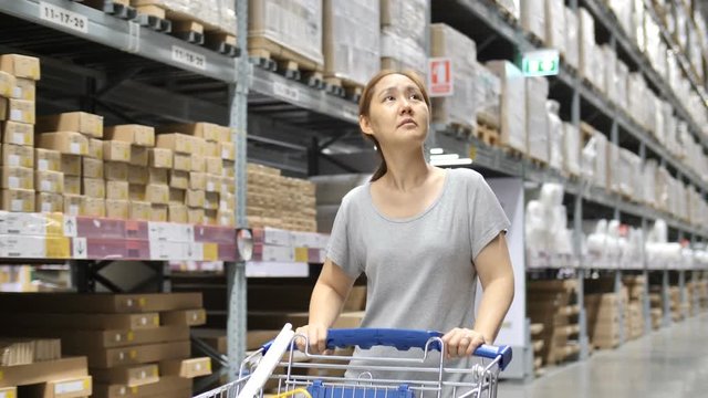4K Slow motion Asian woman rides shopping cart through the warehouse, Choosing new furniture, Tilt up