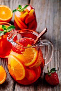 Homemade red wine sangria with orange, apple, strawberry and ice in pitcher  and glass on wooden background