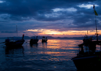 Colorful seascape with traditional thai boats at sunset beach, scenic clouds and shadowy mountains...