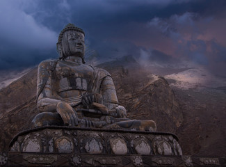 Epic view from the bottom of huge  Buddha statue sitting in lotus pose and snowy peak background covered by colorful thundercloud. Nearby Muktinath temple, Nepal.