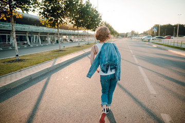 Back view shot of a young woman with short blonde hair and jeans clothes walking on the road in the street. Sunset