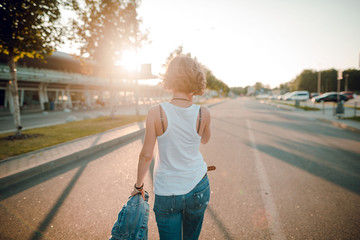 Rear view of a blonde woman with short hair in jeans clothes walking in the street. Sun rays, sunset