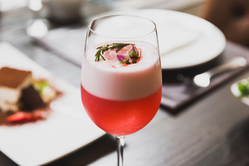 Red cocktail in wine glass topping with foam, flowers and rosemary.