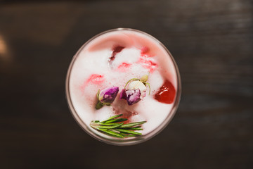 Red cocktail in wine glass topping with foam, flowers and rosemary.