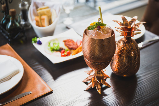 Cocktail served inside copper pineapple cup with dishes in the background.    