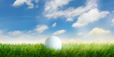 Golfball liegt im Gras vor blauem Himmel mit weissen Wolken, Nahaufnahme