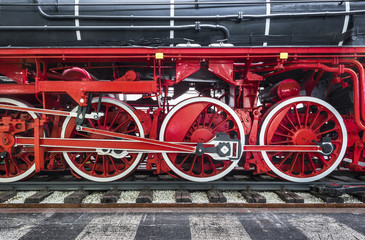 Fototapeta na wymiar Close-up of black heritage steam train on railway tracks with red wheels and transmission engine