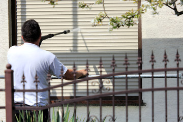 Robotnik, malarz myje karcherem ścianę, fasade budynku mieszkalnego stojąc na rusztowaniu.