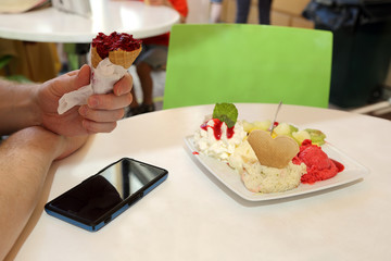 Mężczyzna z telefonem je lody w restauracji. - obrazy, fototapety, plakaty