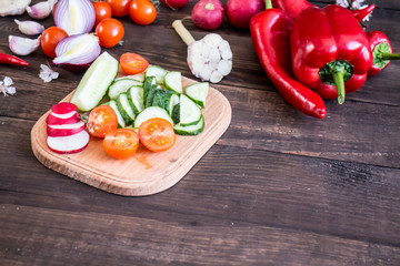 Tomatoes, cucumbers, onions, radish, garlic, pepper, dill, garlic and mushrooms on a dark wooden background.