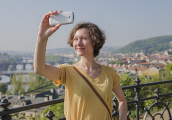 A female tourist makes a photo on a mobile phone in the background of Prague. Tourism in Europe, a woman is walking around the city with a mobile phone