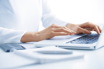 Typing on laptop keyboard. Close-up of a young woman holding brush in her hand and applying makeup. Isolated on light blue background.
