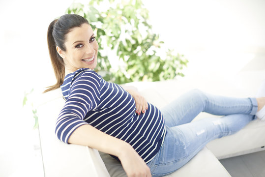 Woman enjoys her pregnancy. Full length shot of beautiful pregnant woman sitting on sofa while relaxing at home.