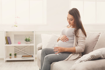 Pregnant woman drinking water sitting on sofa