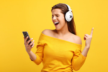 Beautiful woman listening to music on smartphone over yellow background