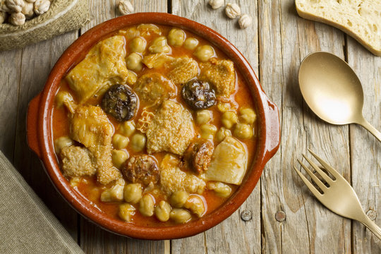 Spanish callos with chickpeas on a wooden table with golden spoon and fork