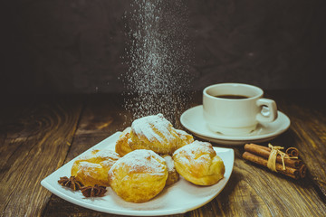 Delicious eclairs sprinkled with icing sugar, stand on a wooden table. Copy spase.