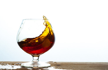 Glass of brandy or cognac splash on the wooden and white background with copy space