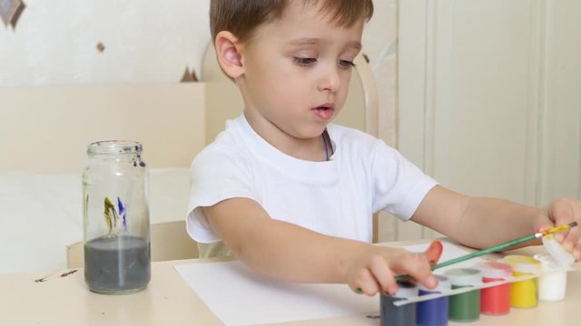 Child boy draws drawings on a white sheet of paper with gouache. Close-up.