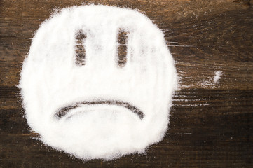 Face of a sad smiley made with granulated sugar. The picture illustrates the harm of eating sugar and salt, as well as dependence on flavoring additives.