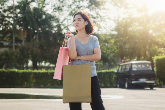 Happy young Asian woman shopping an outdoor market with background of pastel buildings and blue sky. Young asian woman smile with a colorful bag in her hand. Outdoor woman lifestyle shopping concept.