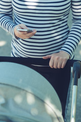 Mother using mobile phone while pushing baby stroller