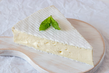 Fresh Brie cheese on white wooden board.