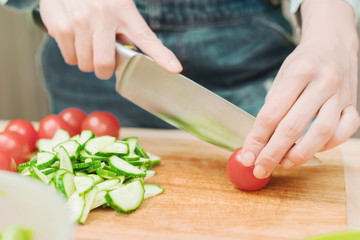 Close-up Delicate female hands cut a large knife with tomatoes on a quarter on a wooden board at home. Home kitchen. Healthy eating. The concept of vegetarianism