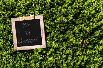Schild an einem Busch mit der Aufschrift -Bin im Garten-. Die Gartenzeit beginnt.