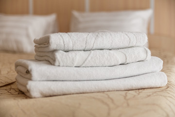 Stack of white hotel towel on bed in bedroom interior.