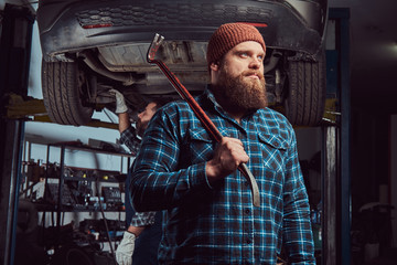 Fototapeta premium Two bearded brutal mechanics repair a car on a lift in the garage. 