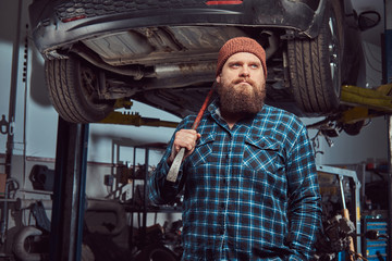 Two bearded brutal mechanics repair a car on a lift in the garage. 