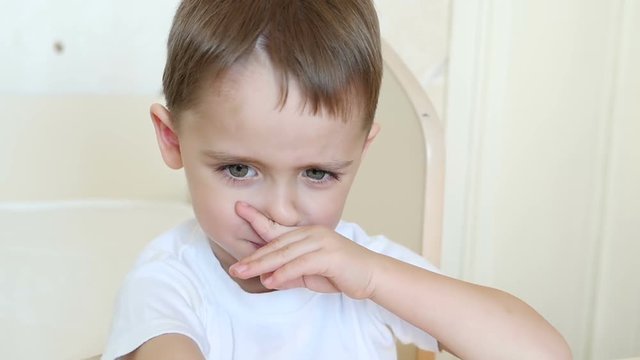 A close-up of a child looks at the camera, frowning. The boy shows discontent, disappointment, negative emotions, closes his nose with his finger