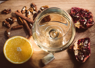 A glass of white wine as the central element of the composition surrounded by orange, nuts and pomegranate.
