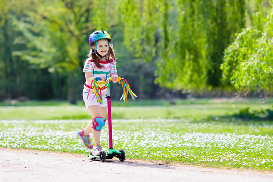 Child riding kick scooter in summer park.