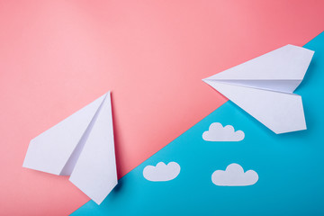 White paper origami airplane with clouds lies on pastel blue background
