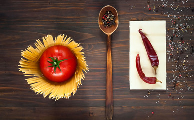 wooden spoon with spices and fresh red tomato, surrounded by spaghetti on a wooden background, close-up, top view, concept of cooking italian pasta, copy space, minimalism