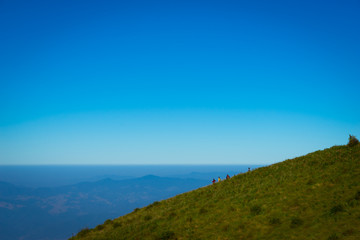 A group of people with backpacks walking along the road. There are mountains on the horizon. The sky is blue and cloudy.