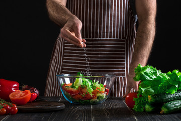 Man preparing healthy salad of fresh vegetables on a wooden table.
