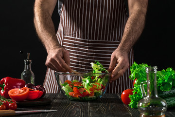 Man preparing salad with fresh vegetables on a wooden table. Cooking tasty and healthy food