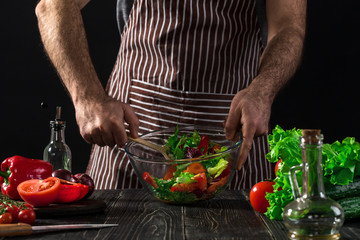 Man preparing salad with fresh vegetables on a wooden table. Cooking tasty and healthy food